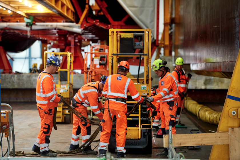 Arbejdere i orange arbejdstøj arbejder i tunnel fabrikken.