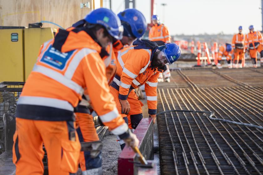 Arbejdere i orange arbejdstøj arbejder med armeringsstål.