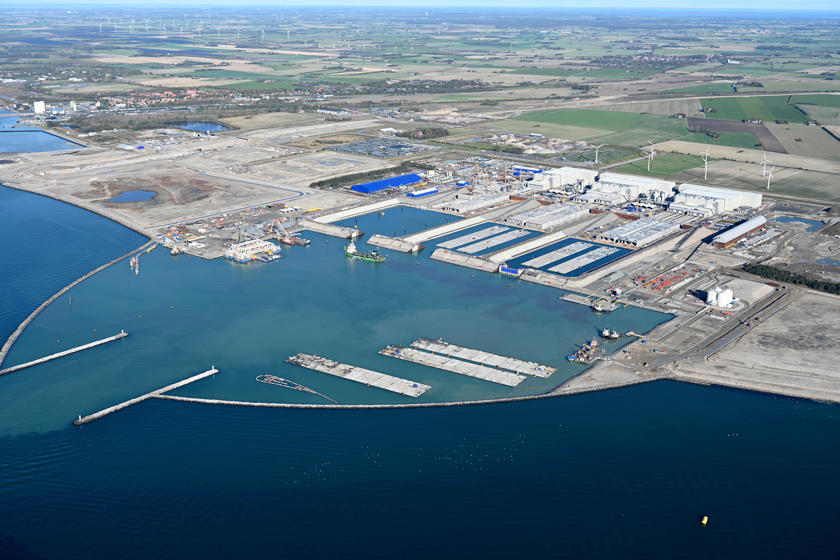 Tunnelelementfabrikken i Rødbyhavn. I de tre store hvide haller produceres betonelementer. I bassinerne og i arbejdshavnen foran fabrikshallerne flyder færdige elementer i vandet.