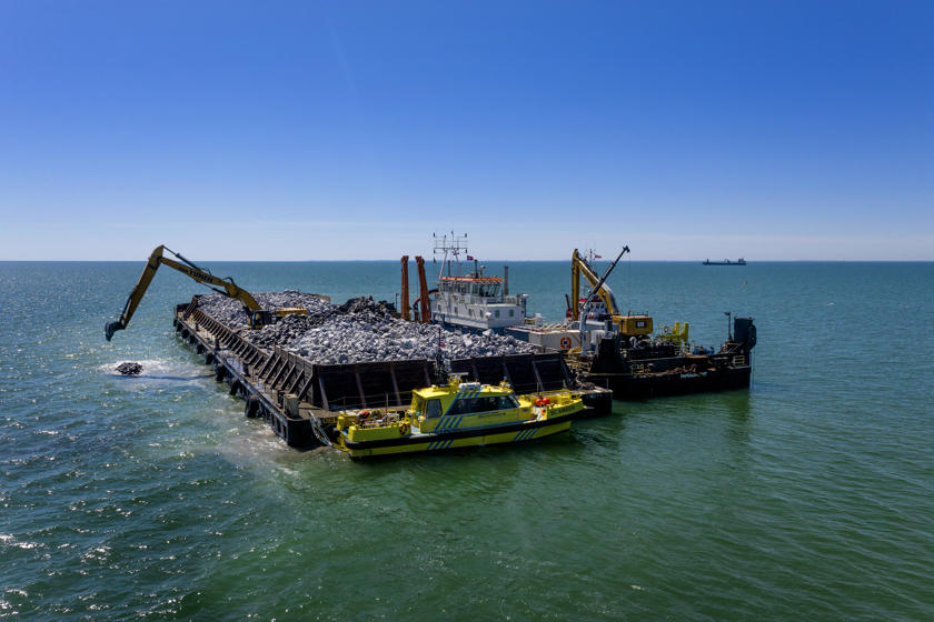 Eine Schute mit Granit für die Wellenbrecher im Fehmarnbelt. Bagger versenken die Granitbrocken im Meer, um die Wellenbrecher zu errichten.