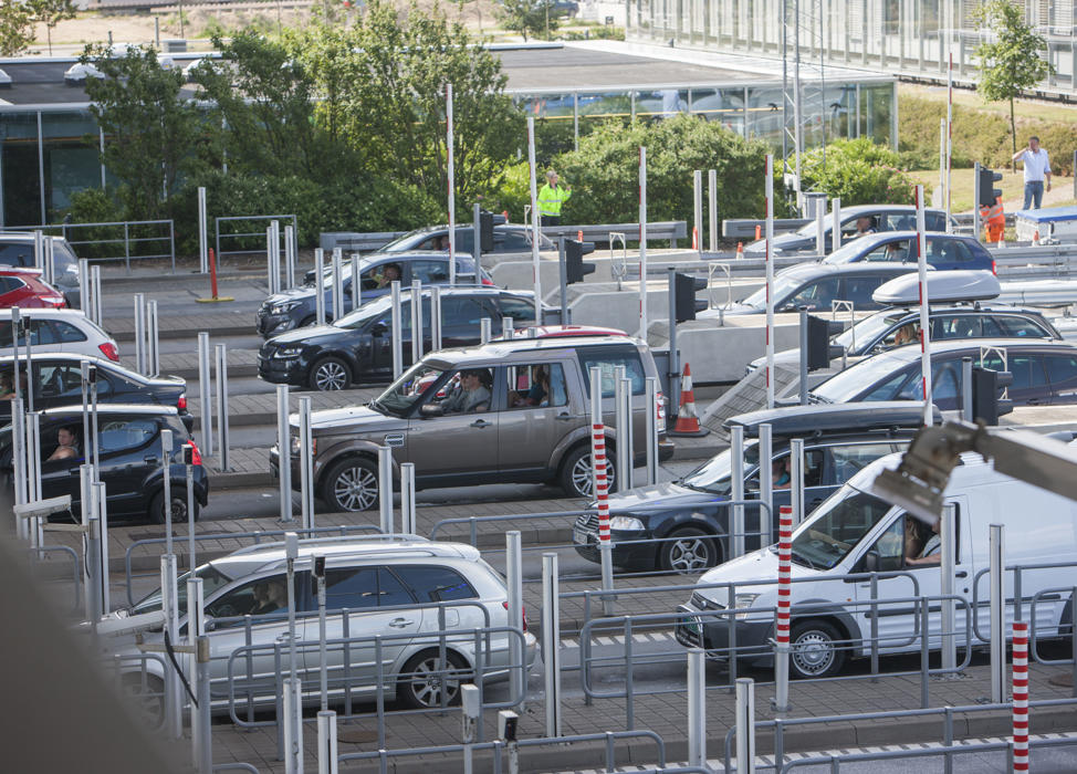 En række biler holder ved en betalingsstation for at betale vejafgiften foran de rød-hvide bomme.