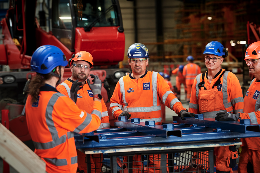 Arbejdere i orange arbejdstøj får en forklaring af formanden i tunnelfabrikken.