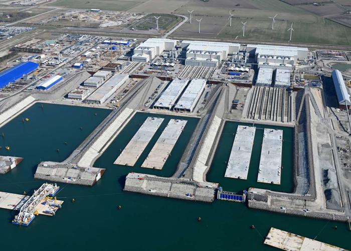 Luftaufnahmen der Tunnelfabrik bei Rødbyhavn, auf denen die Tunnelelemente im Wasserbecken, die Produktionshallen und eines der IVY-Spezialschiffe zu sehen sind.