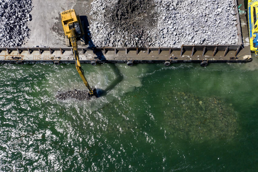 An excavators drops boulders into the sea to construct breakwaters.