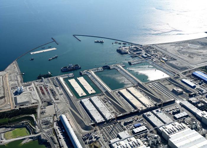 Aus den Produktionshallen schauen Elemente heraus. Vor den Hallen liegen Elemente, die weiter ausgestattet werden. In den Becken und im Hafen schwimmen fertige Elemente.