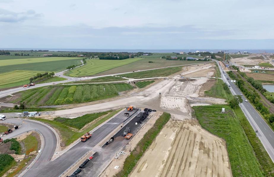 Das Luftbild zeigt wie derzeit noch der Verkehr auf der bestehenden B207 zum Fährhafen Puttgarden rollt. Die neue Anbindung des Fährhafen verläuft weiter westlich und steht kurz vor der Inbetriebnahme.