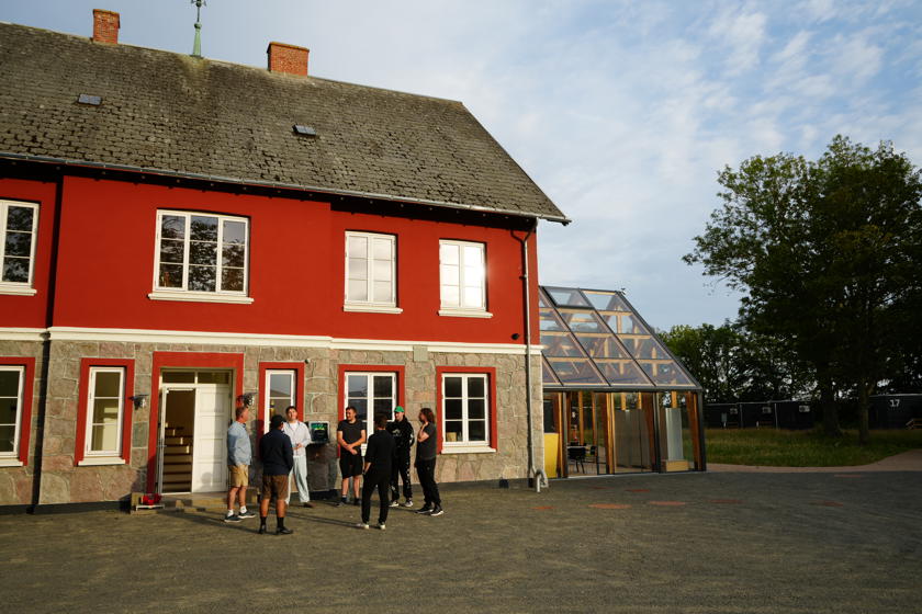 Det røde toetagers hovedhus på Campus Femern med mange vinduer. På siden er der tilbygget en vinterhave.